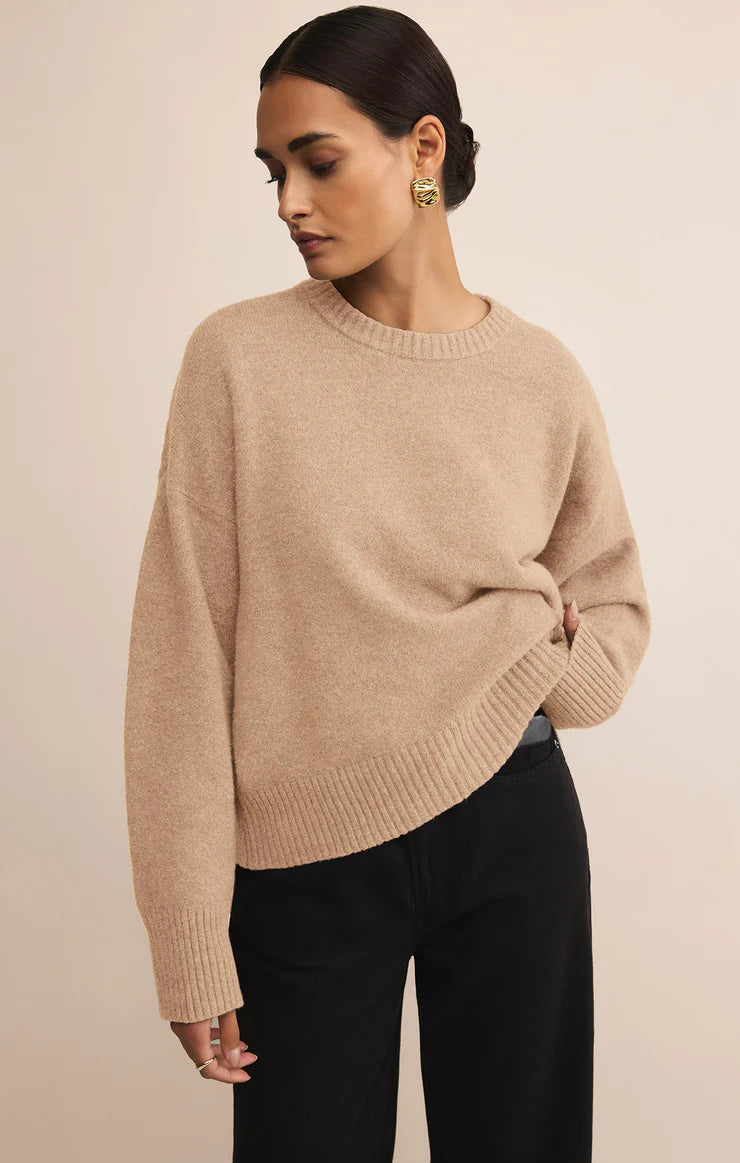 Woman wearing a beige sweater and black pants against a beige background