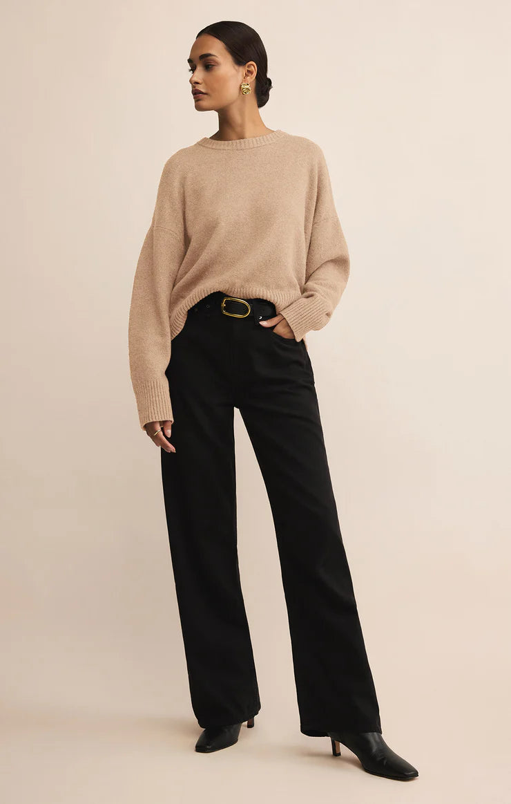 Woman wearing a beige sweater and black pants on a beige background