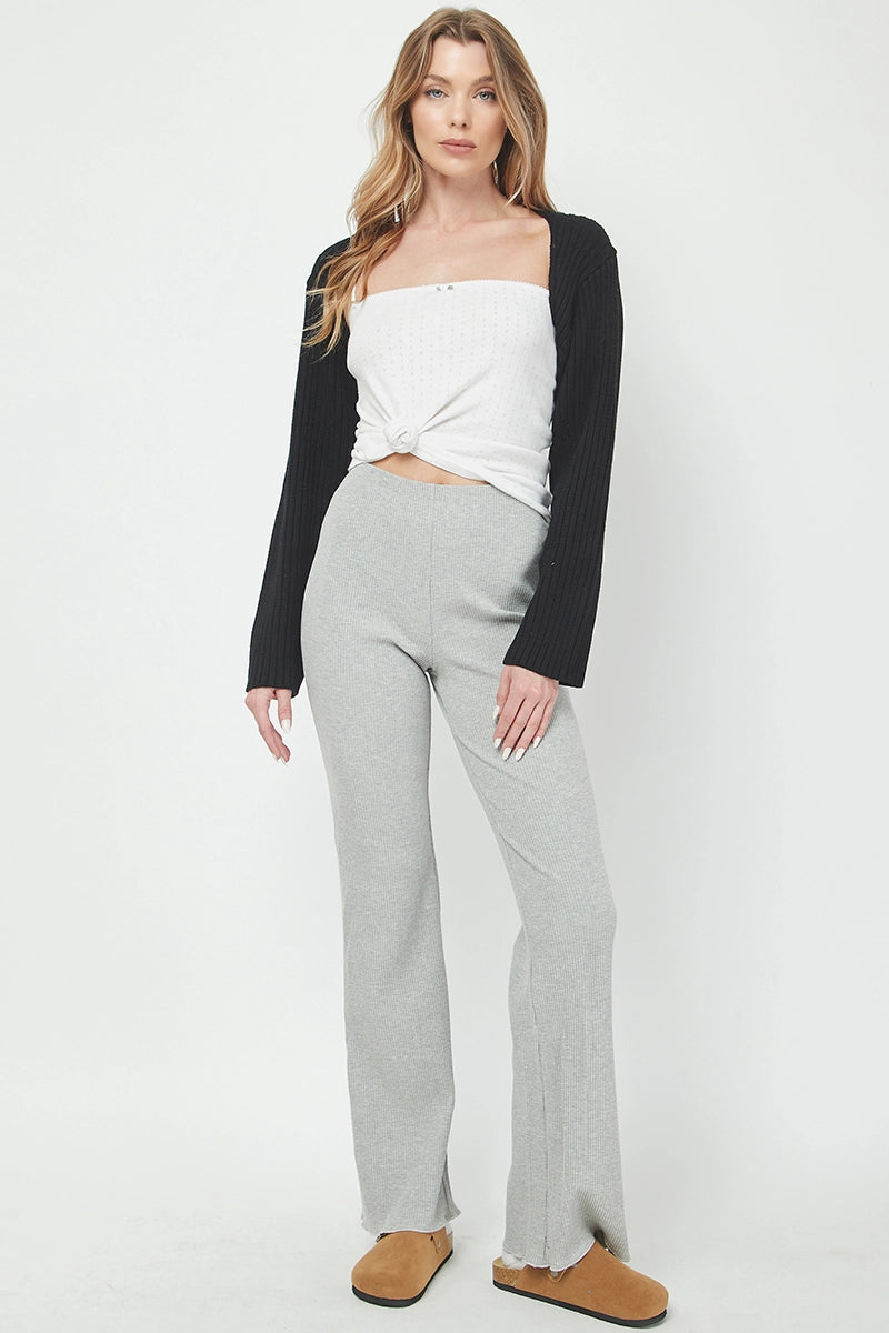 Woman wearing a black cardigan over a white top and gray pants on a white background