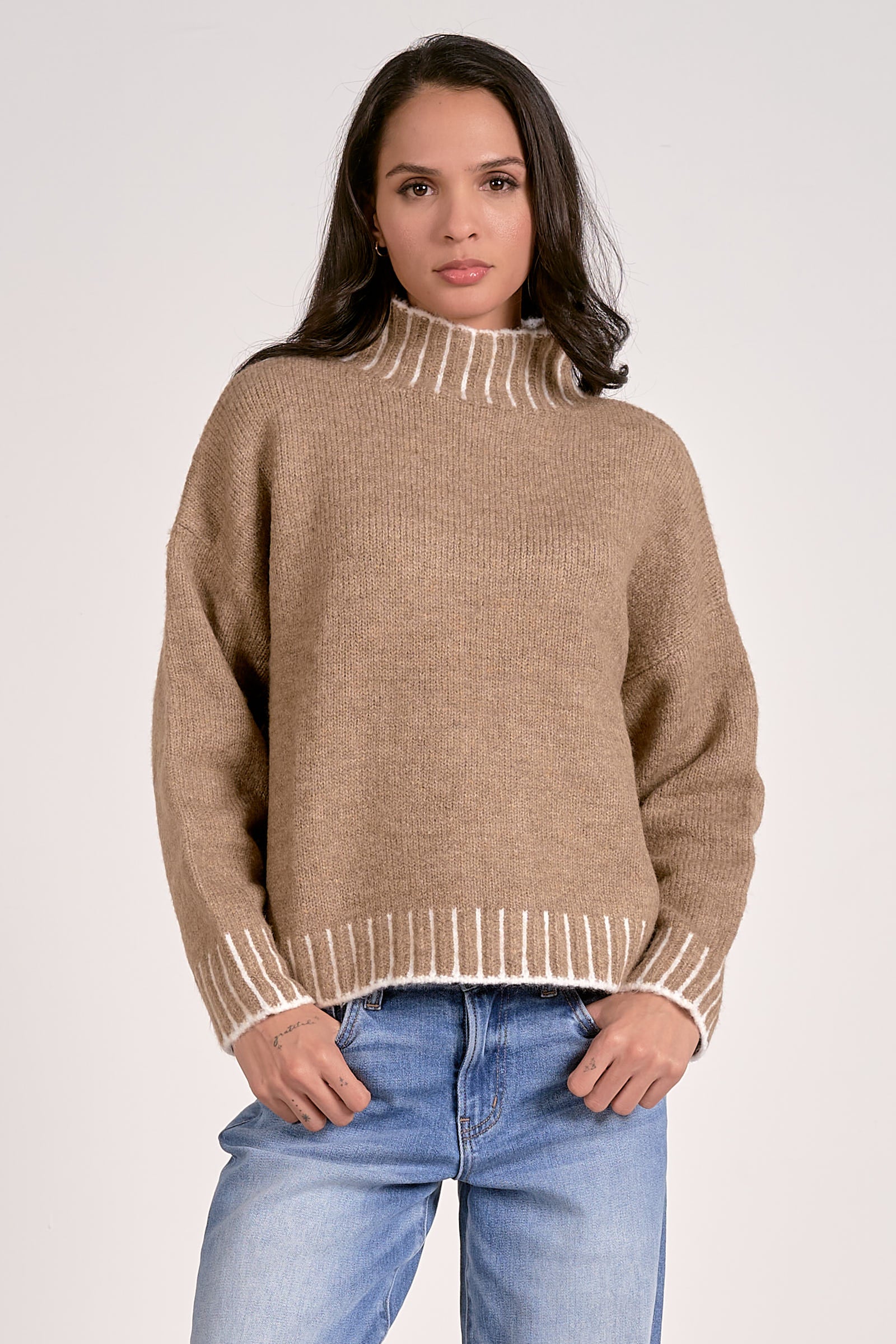 Woman wearing a beige sweater with white trim on a plain background