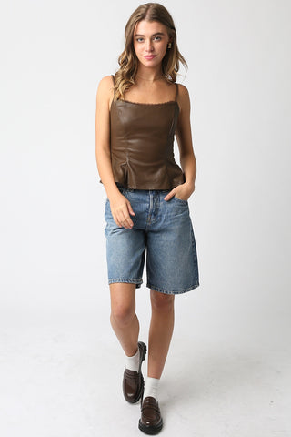 Woman wearing a brown leather tank top and denim shorts on a white background