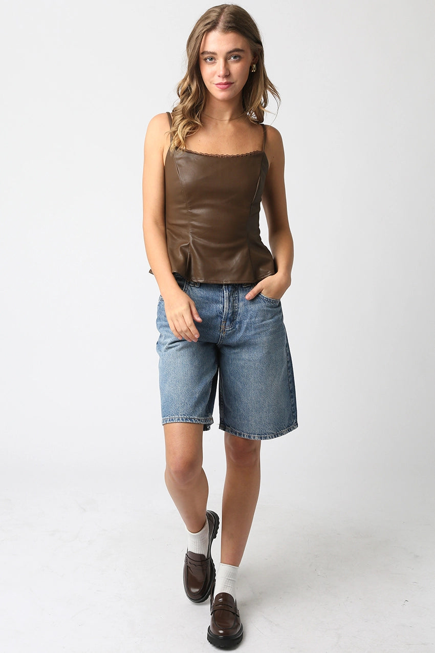 Woman wearing a brown leather tank top and denim shorts on a white background