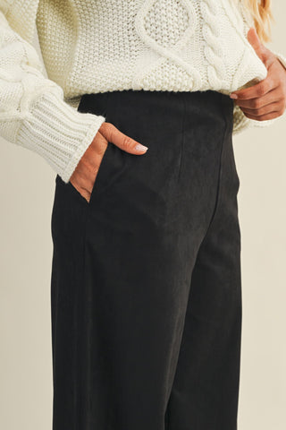 Person wearing a white cable knit sweater and black pants against a neutral background