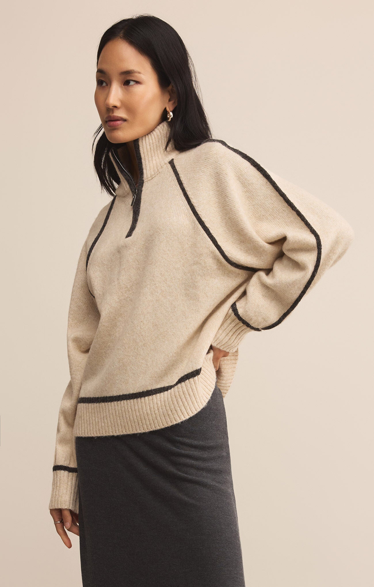 Woman wearing a beige sweater with black accents on a beige background