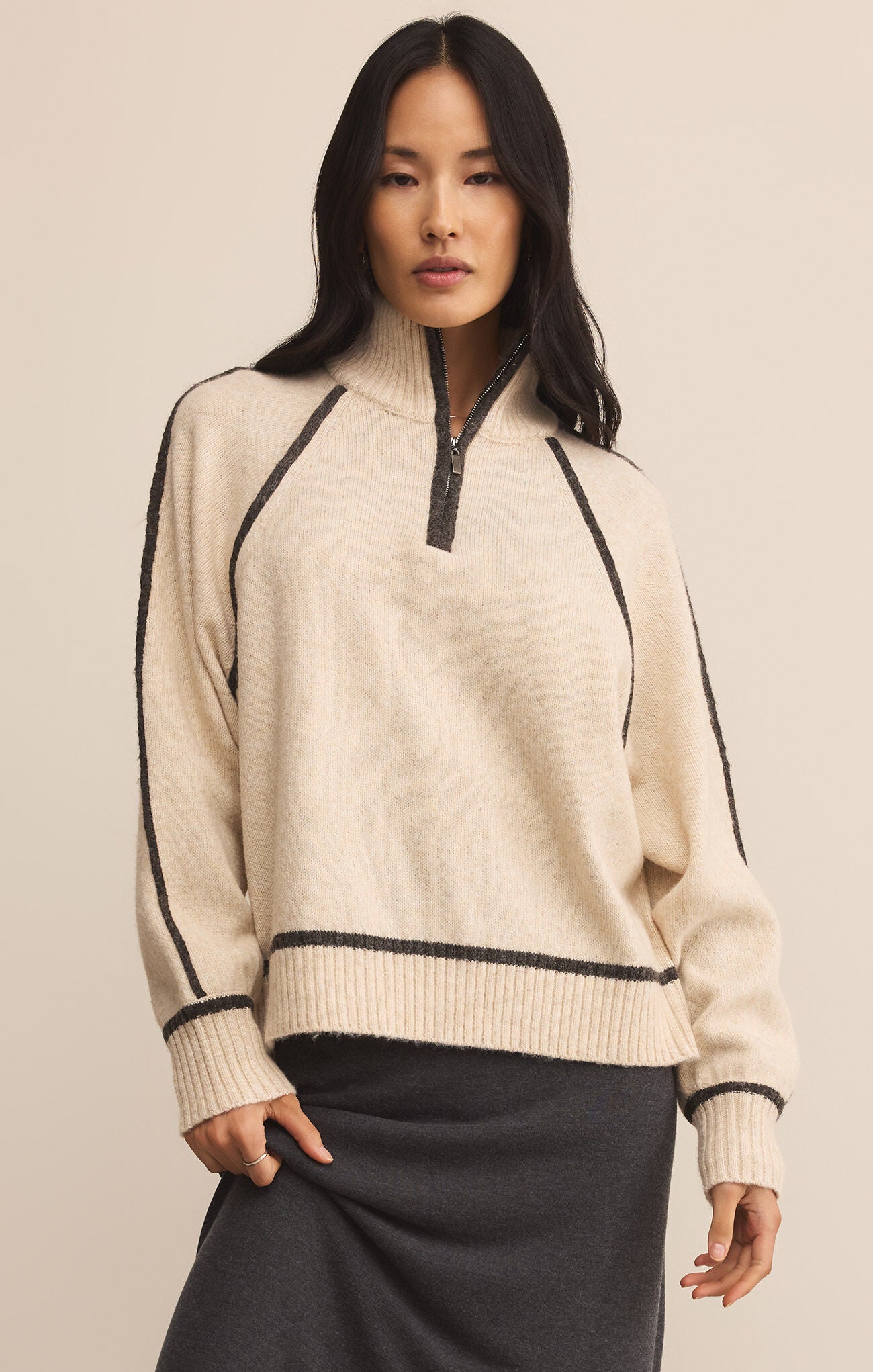 Woman wearing a beige sweater with black accents on a beige background