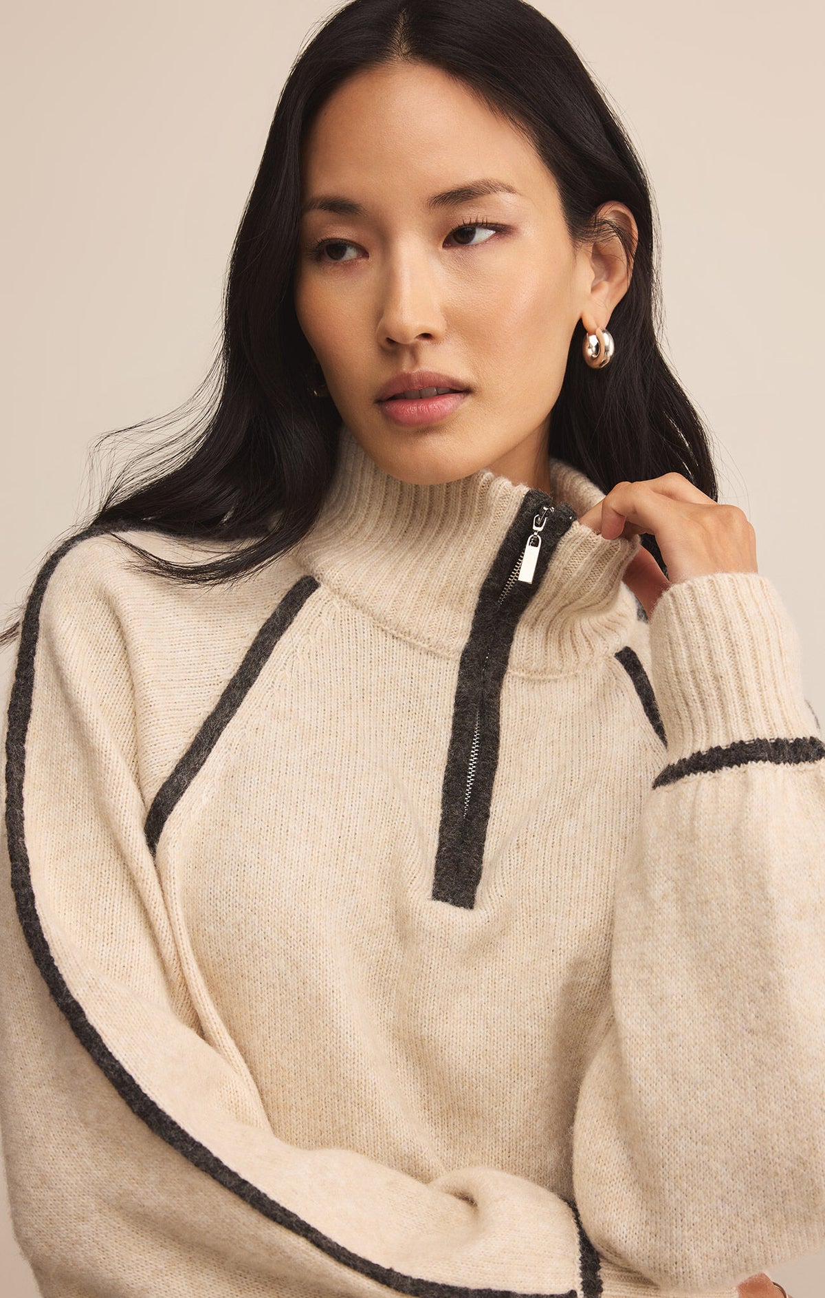 Woman wearing a beige sweater with black accents on a plain background