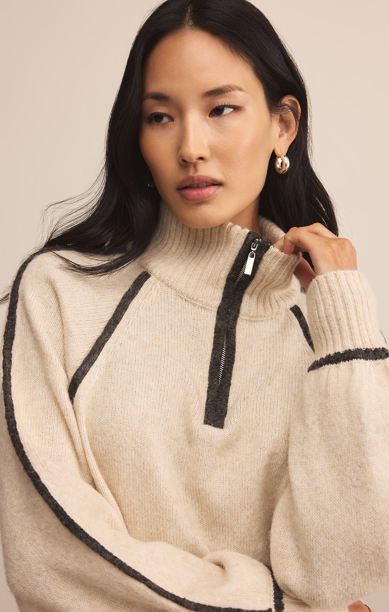Woman wearing a beige sweater with black accents on a plain background