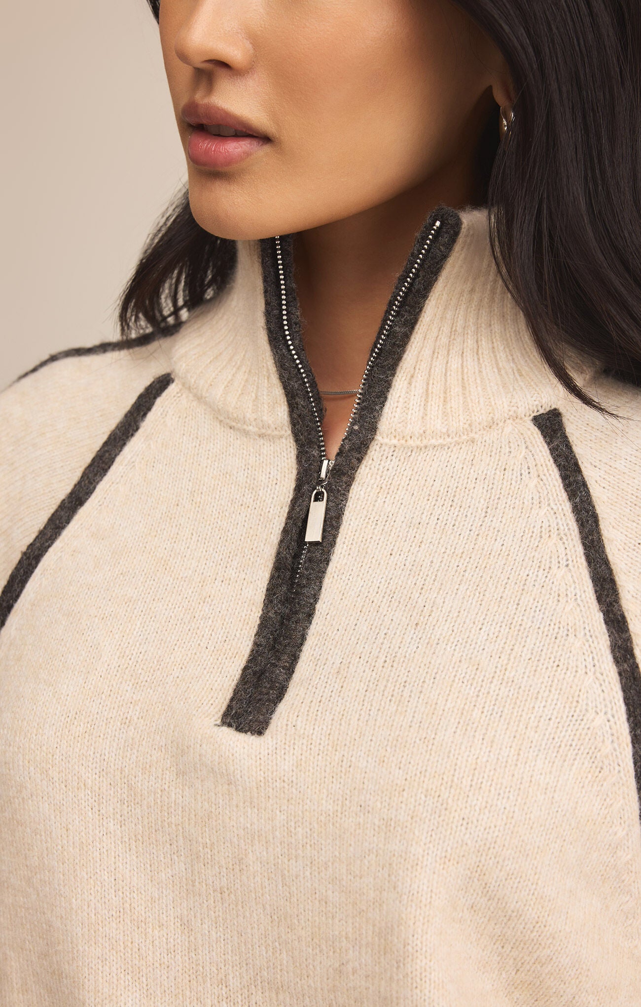 Close-up of a person wearing a beige sweater with black ribbed trim and zipper.