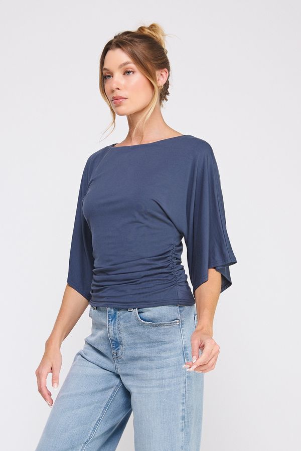 Woman wearing a navy blue top with wide sleeves and light blue jeans on a white background