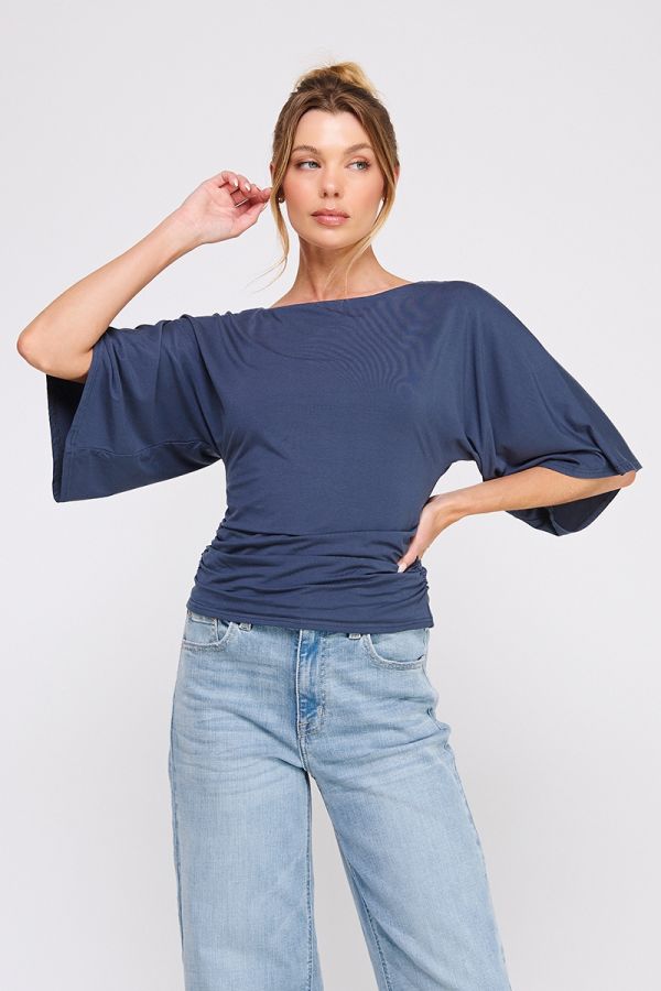Woman wearing a navy blue top with wide sleeves and light blue jeans on a white background