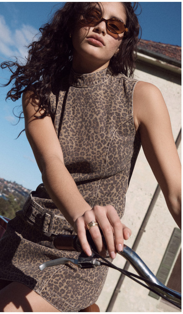 Woman in a leopard print dress sitting on a bicycle with a scenic background