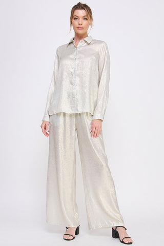 Woman wearing a light-colored blouse and wide-leg pants on a white background