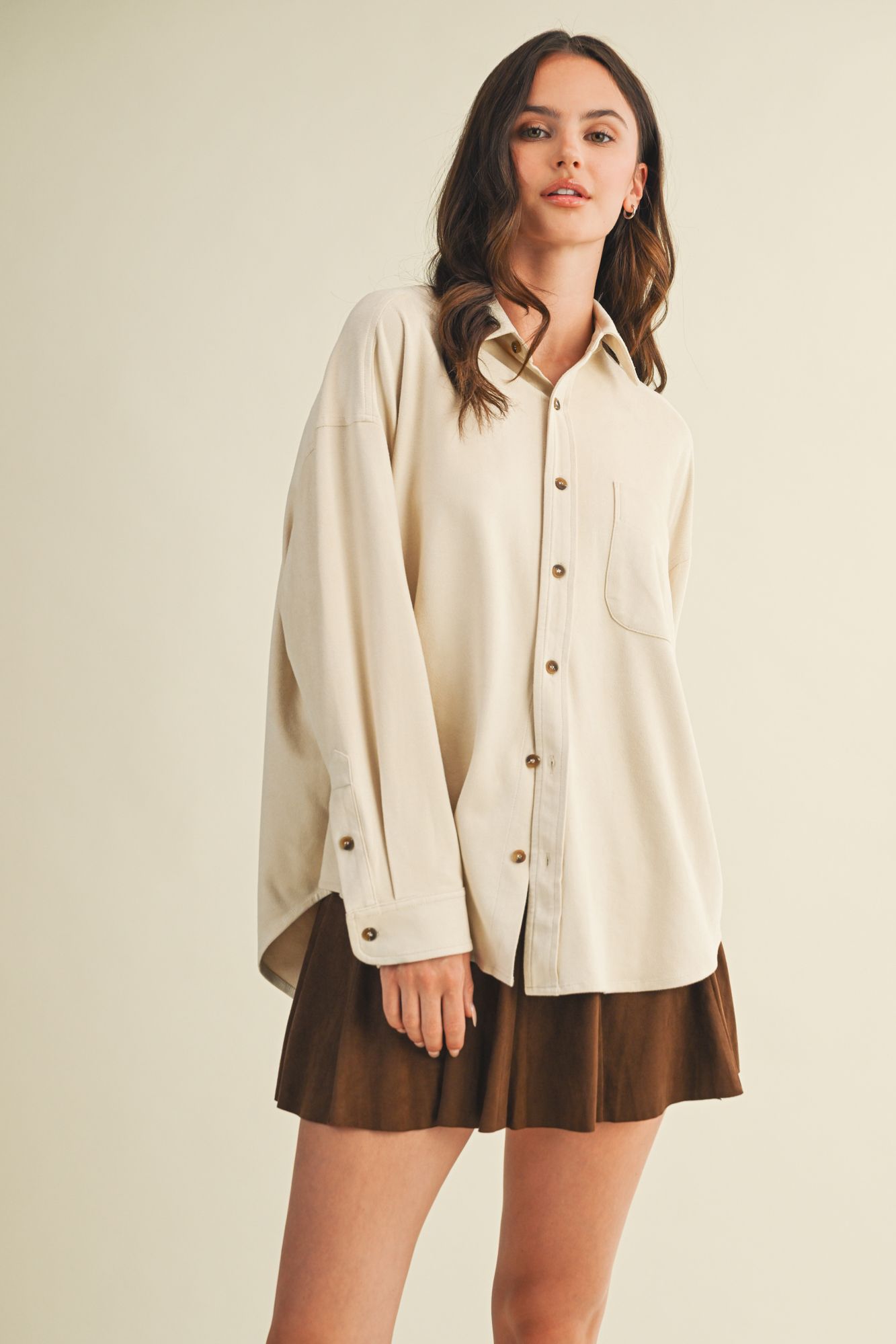 Woman wearing a beige oversized shirt and brown skirt on a plain background