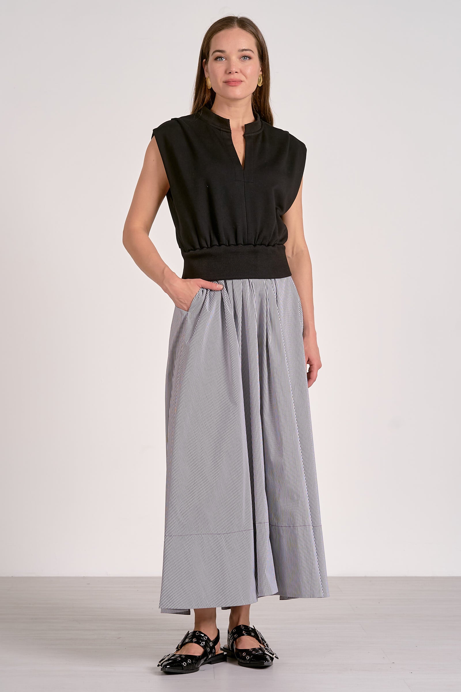 Woman wearing a black sleeveless top and gray wide-leg pants on a white background