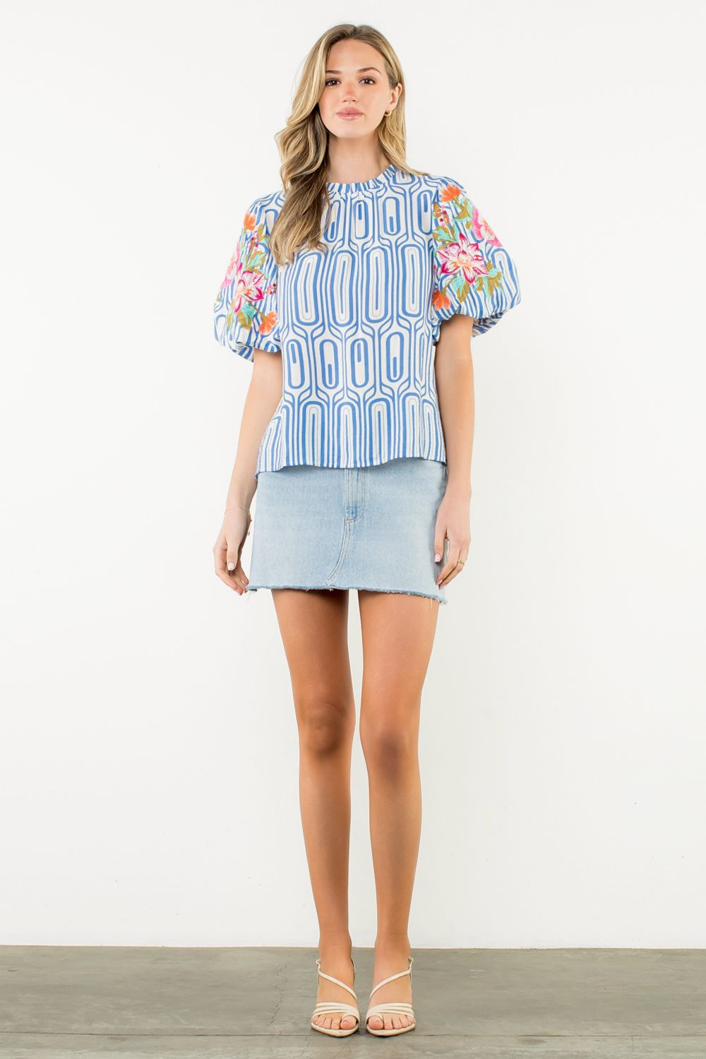 Woman wearing a colorful embroidered top and denim skirt on a white background