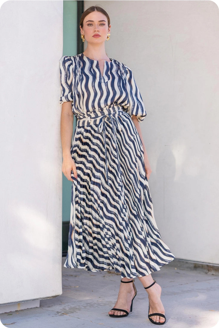 Woman wearing a blue and white striped dress standing against a white wall.