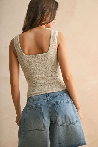 Woman wearing a beige tank top and blue jeans against a beige background