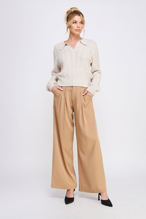 Woman wearing a cream sweater and beige wide-leg pants on a white background