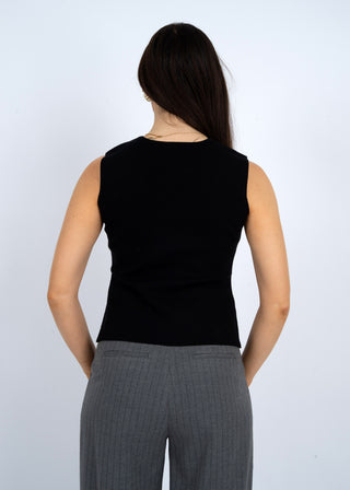 Person wearing a black sleeveless top and gray pants against a white background