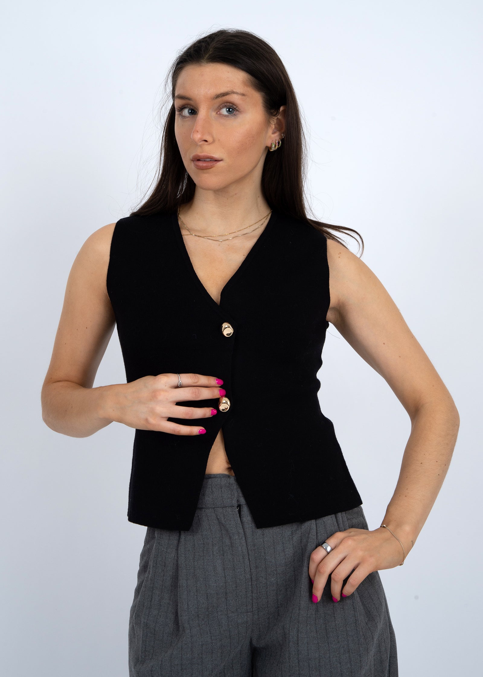 Woman wearing a black sleeveless top with buttons against a white background