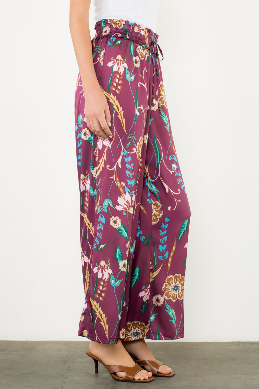 Woman wearing a white sleeveless top and purple floral pants on a white background