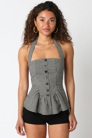 Woman wearing a black and white checkered halter top with buttons on a plain background