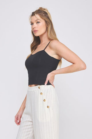 Woman wearing a black top and white pants with gold buttons on a light gray background