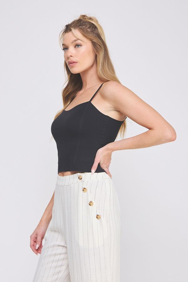 Woman wearing a black top and white pants with gold buttons on a plain background