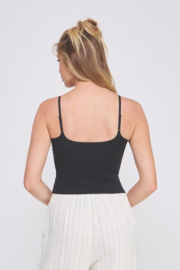 Woman wearing a black tank top and white pants on a plain background