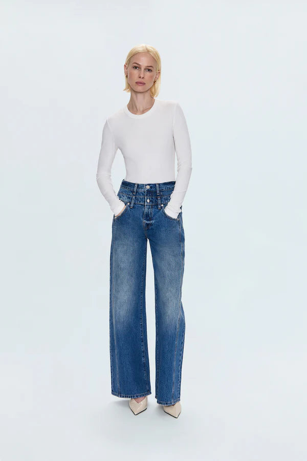 Person wearing a white long-sleeve top and blue jeans on a light gray background