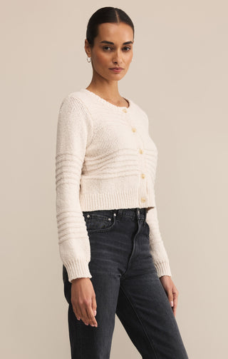 Woman wearing a cream cardigan and dark jeans against a beige background