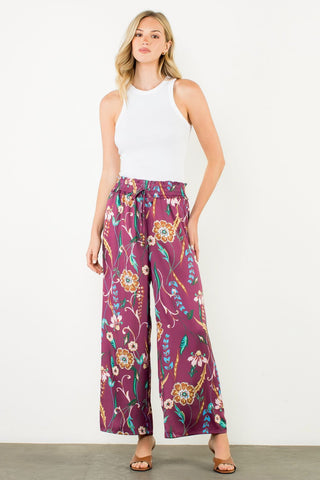 Woman wearing a white sleeveless top and purple floral pants on a white background