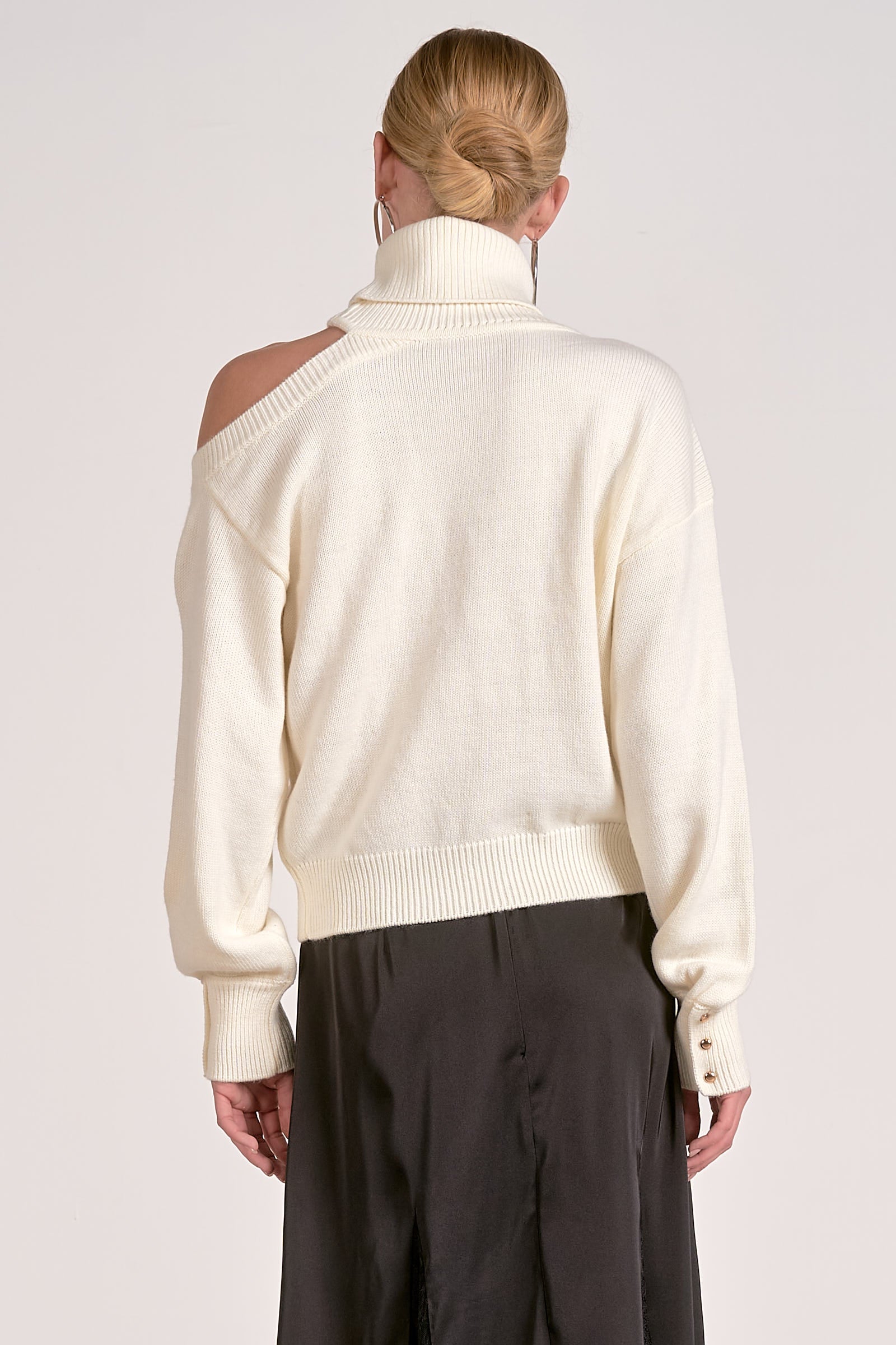 Woman wearing a cream sweater with gold buttons on a white background