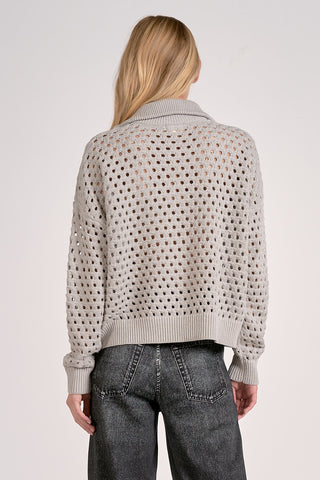 Person wearing a light gray sweater with a textured pattern on a plain background