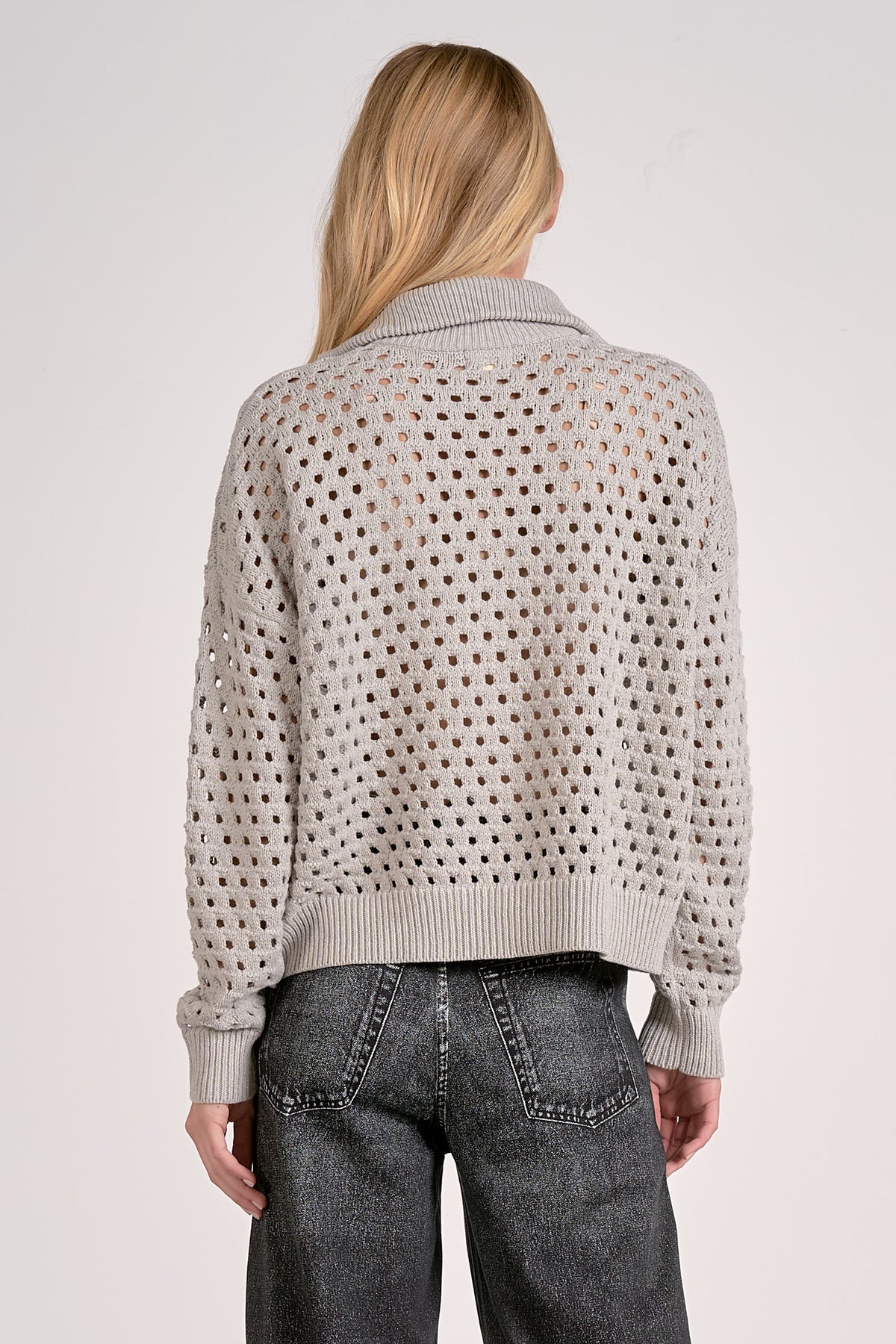 Person wearing a light gray sweater with a textured pattern on a plain background