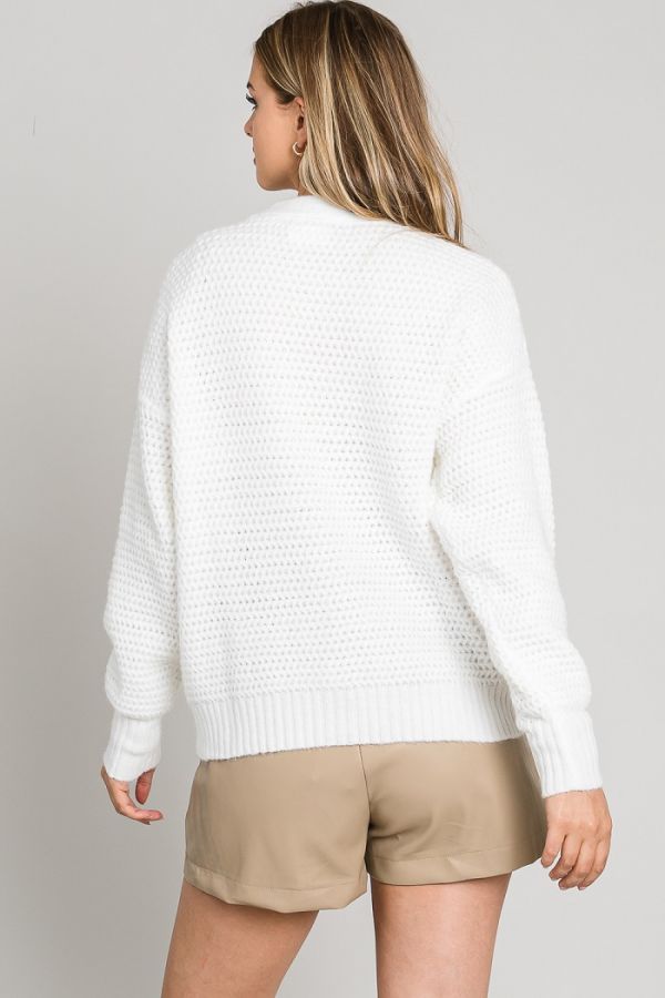 Woman wearing a white textured sweater and beige shorts on a plain background