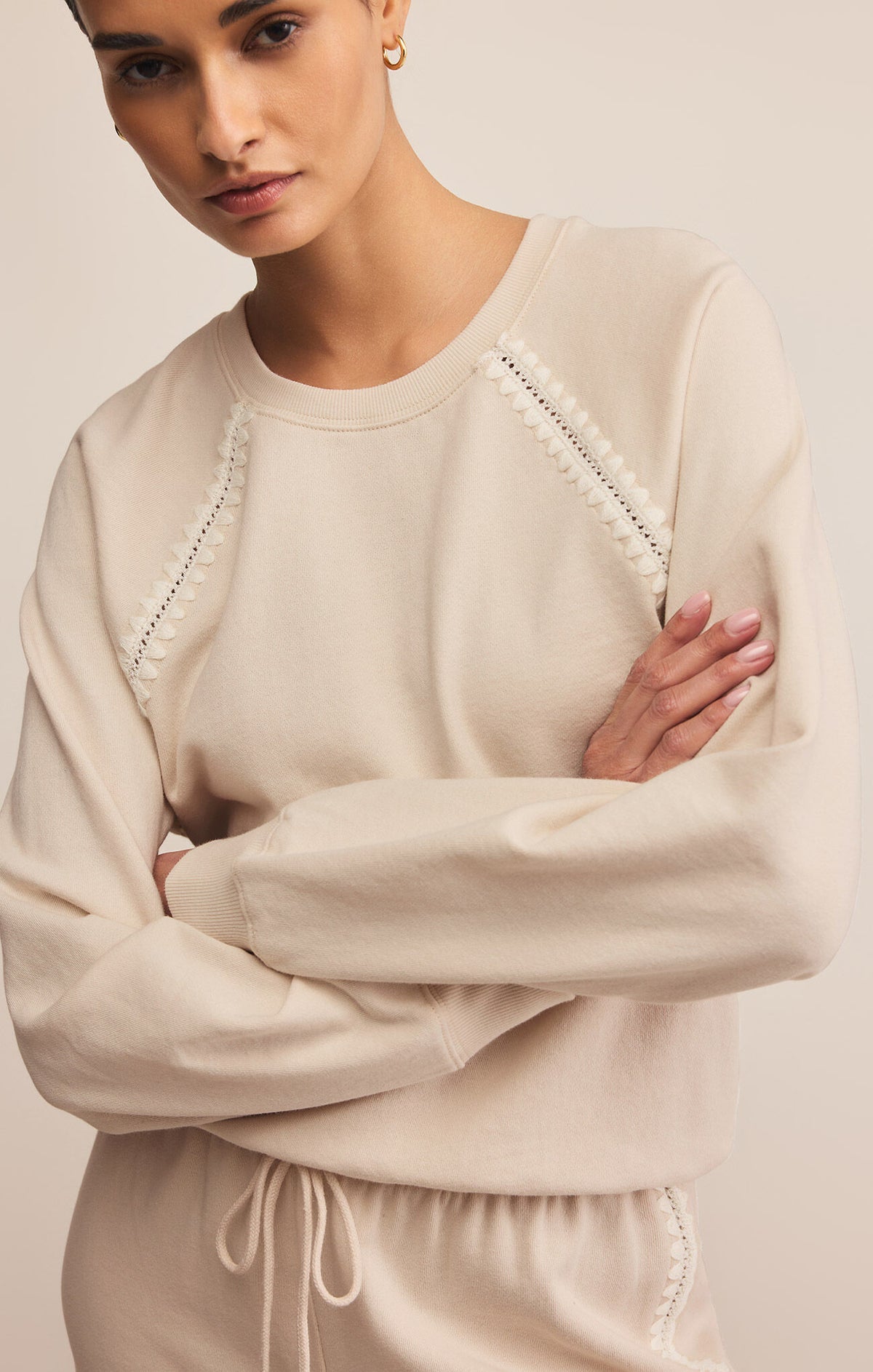 Woman wearing a beige sweater with intricate detailing on a plain background