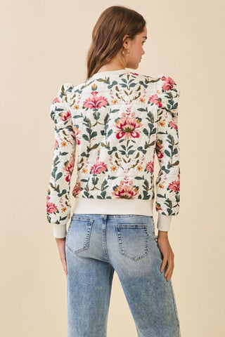Woman wearing a floral embroidered top and jeans on a beige background