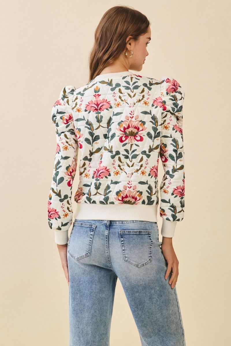 Woman wearing a floral embroidered top and jeans on a beige background