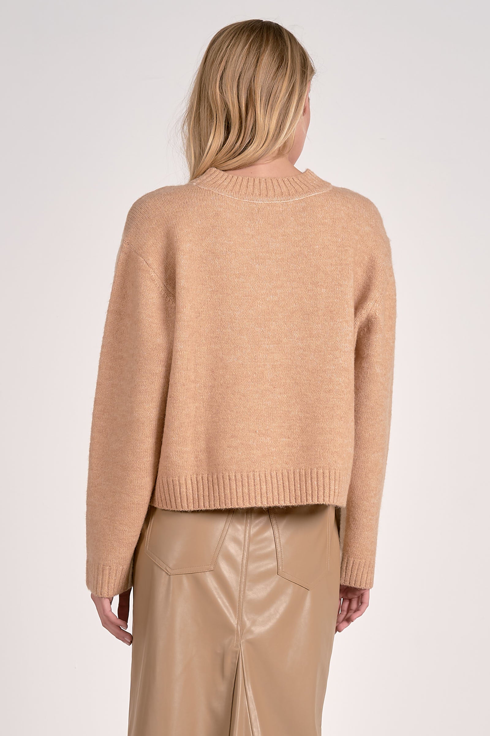 Woman wearing a beige sweater with a gradient effect and beige pants on a white background