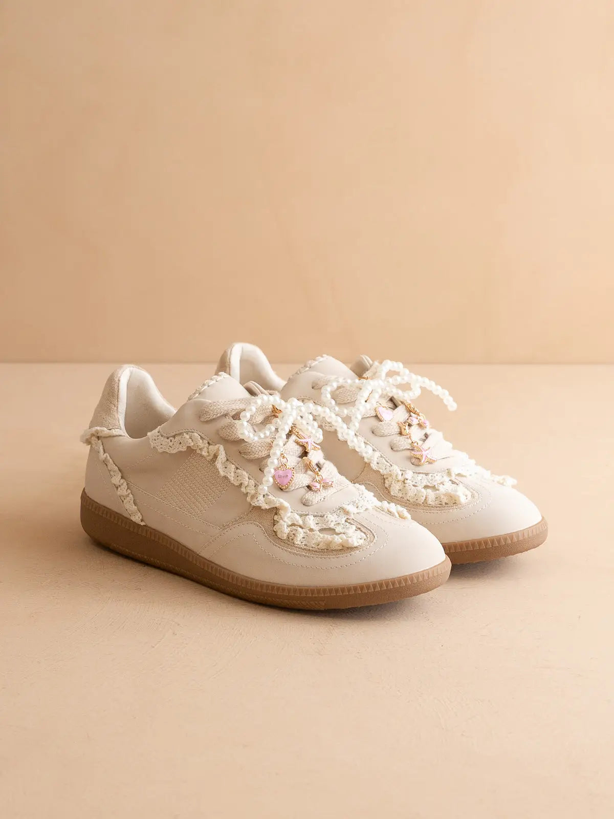 Pair of white sneakers with lace and pearl details on a beige background