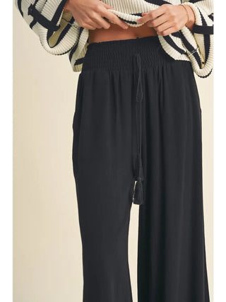 Black wide-leg pants worn with a patterned sweater on a beige background