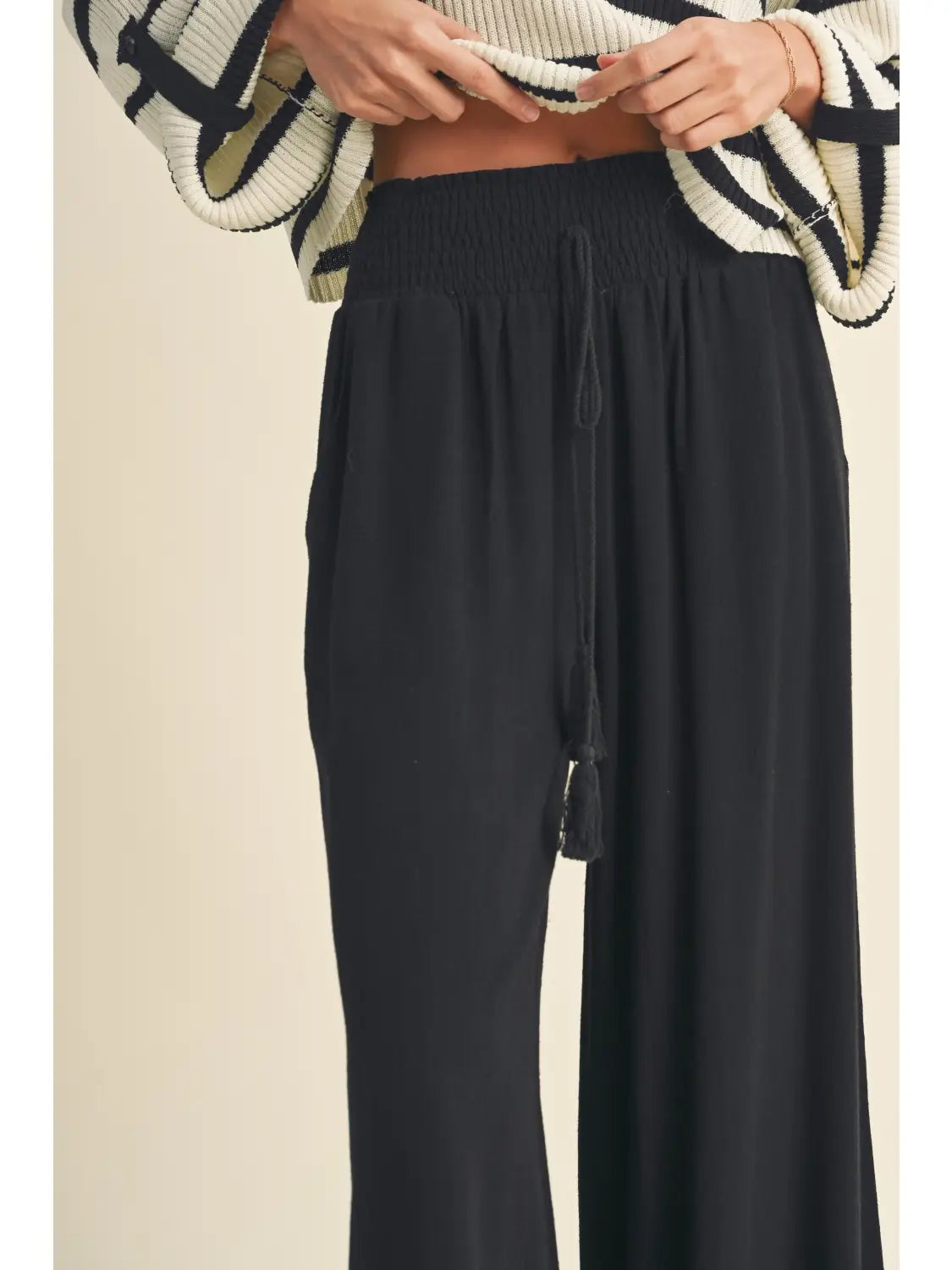 Black wide-leg pants worn with a patterned sweater on a beige background