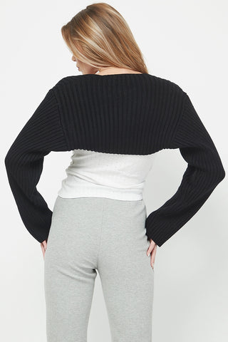 Person wearing a black cropped sweater over a white top and gray pants on a light gray background