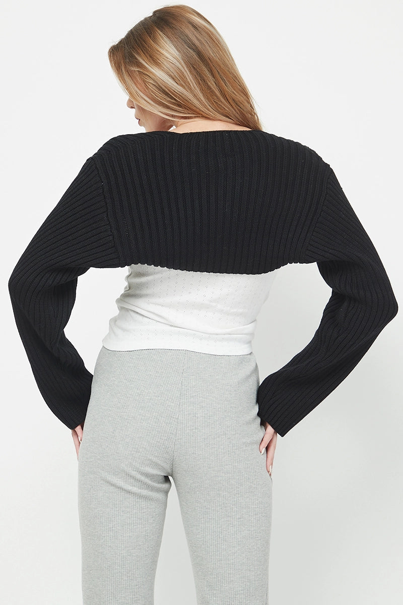 Person wearing a black cropped sweater over a white top and gray pants on a light gray background