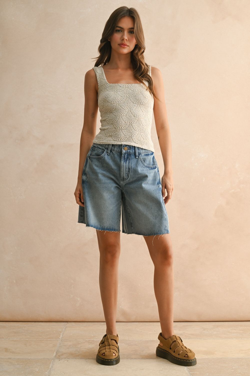Woman wearing a sleeveless top and denim shorts against a beige background