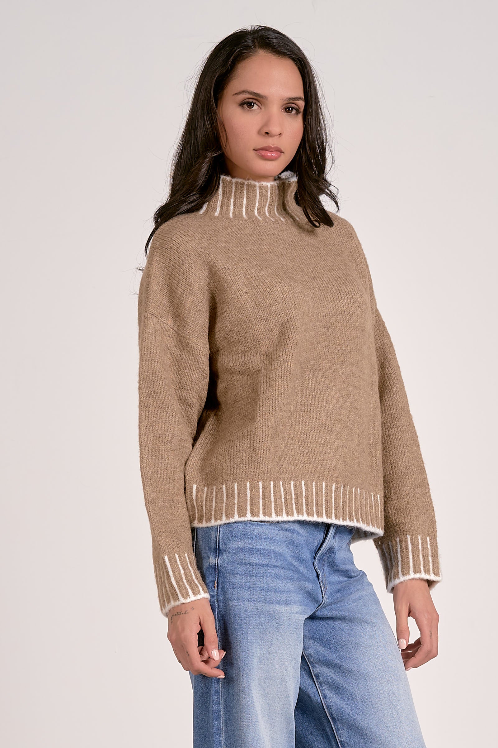Woman wearing a beige sweater with white trim on a plain background