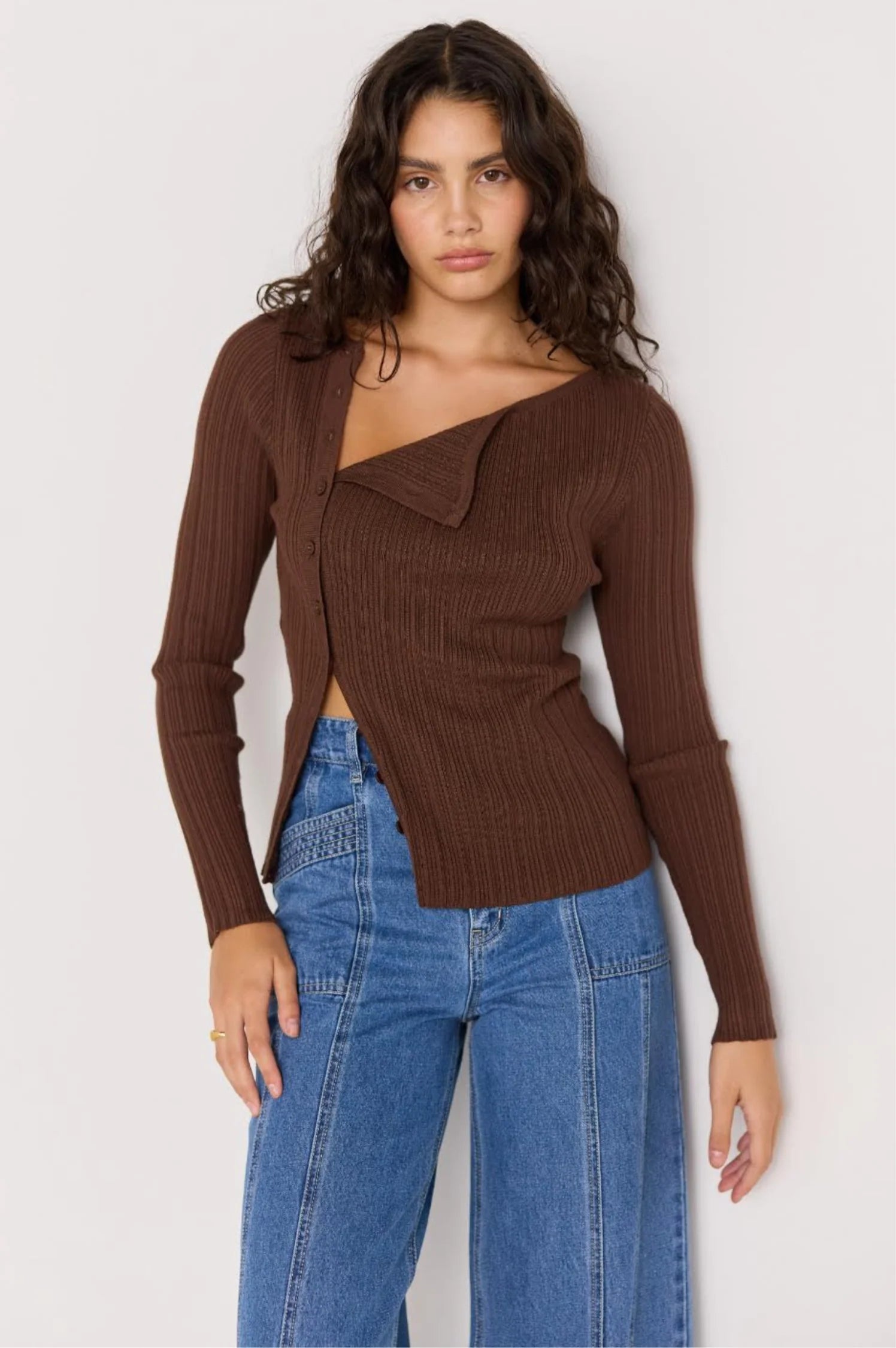 Woman wearing a brown ribbed sweater and blue jeans against a white background