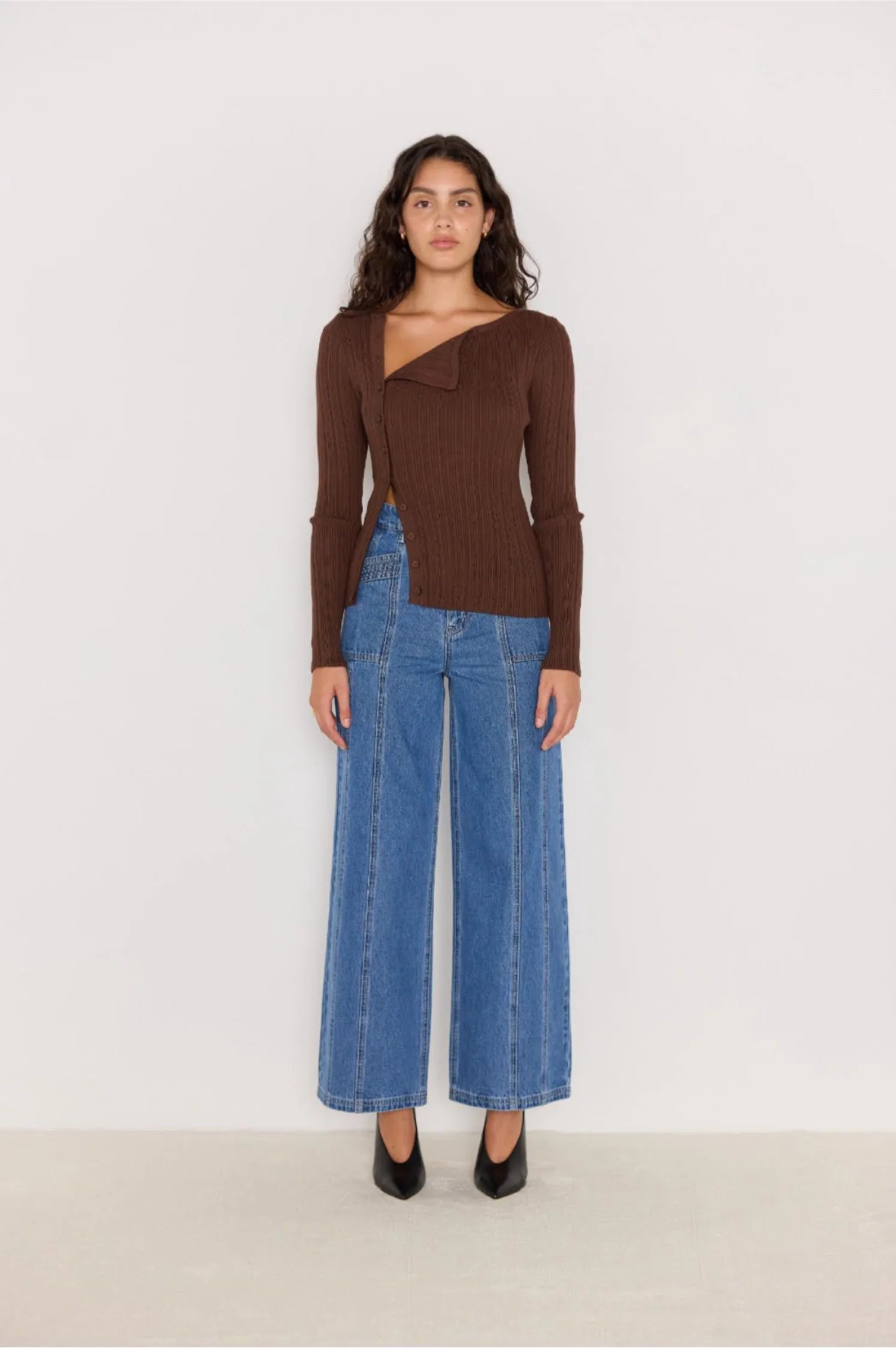 Woman wearing a brown ribbed sweater and blue jeans against a white background