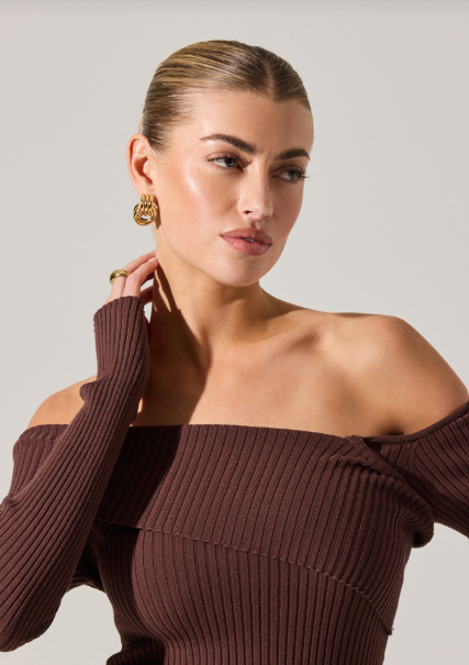 Woman wearing a brown off-shoulder ribbed sweater against a plain background